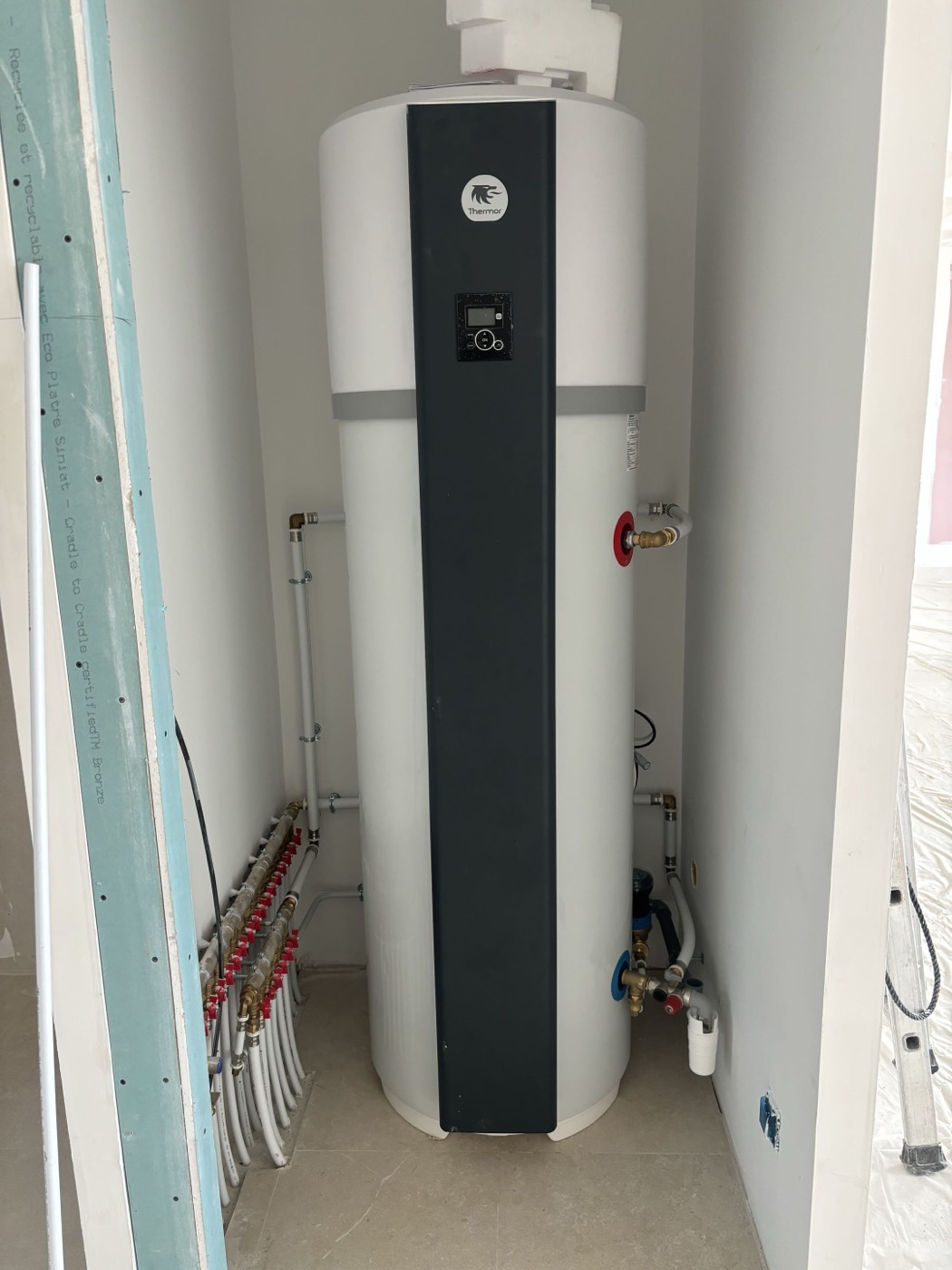 Chauffe-eau thermodynamique installé dans le local technique d'une maison neuve, à côté de la nourrice de distribution