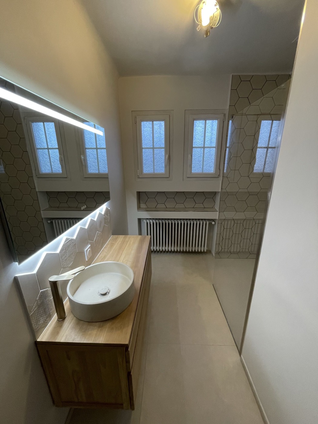 La même salle de bain après rénovation complète : plan en bois massif, vasque à poser, miroir rétroéclairé et douche à l'italienne